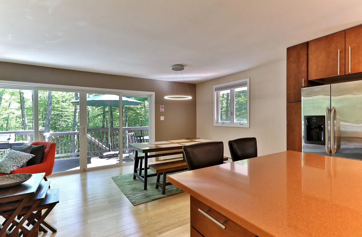 This image showcases an open kitchen and dining area with a kitchen island, a dining table set for meals, and sliding glass doors that open to an outdoor deck. The space is filled with natural light, emphasizing the connection between the kitchen, dining, and living spaces.