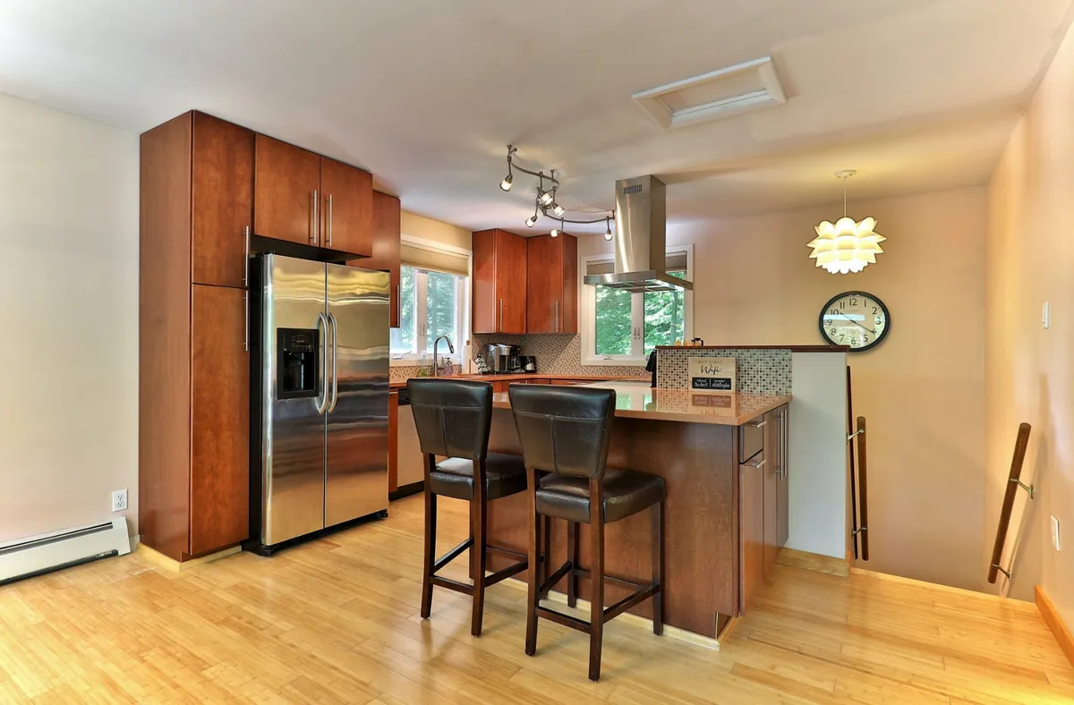 A welcoming kitchen interior featuring a prominent kitchen island, stainless steel refrigerator, and a well-lit cooking area. The space invites group cooking or holiday meal preparation, and the modern appliances are clearly visible.