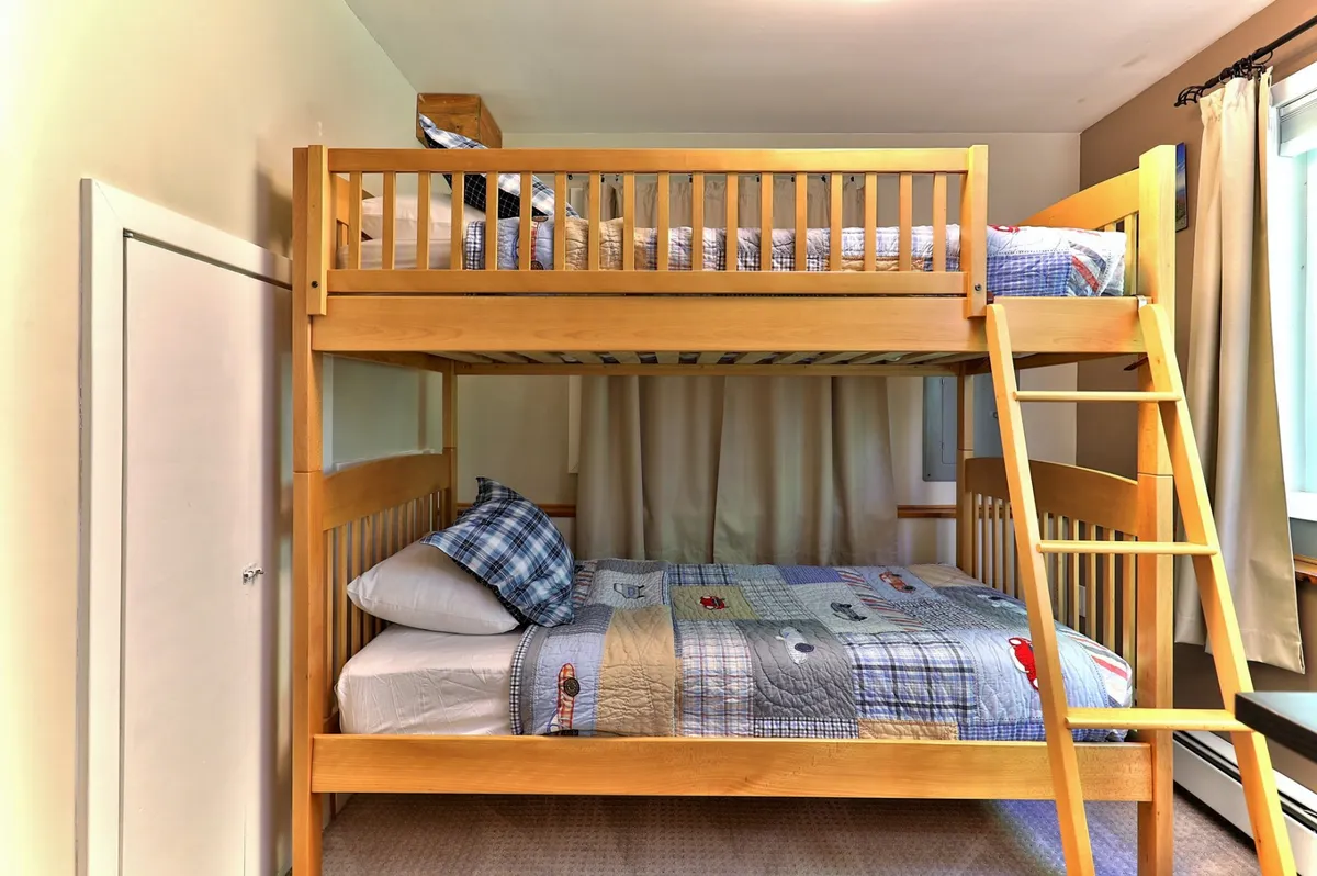 A playful bunk room with a ladder for access, featuring colorful bedding and cozy pillows. The room exudes a fun atmosphere perfect for kids or young-at-heart guests, matching the bunk room description.
