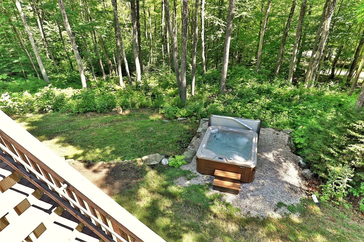 This exterior shot features a steaming hot tub nestled among lush greenery and a gravel pathway, providing a tranquil setting to unwind after a day of skiing or snowboarding. The natural environment hints at the relaxing amenities waiting for guests post-adventure.